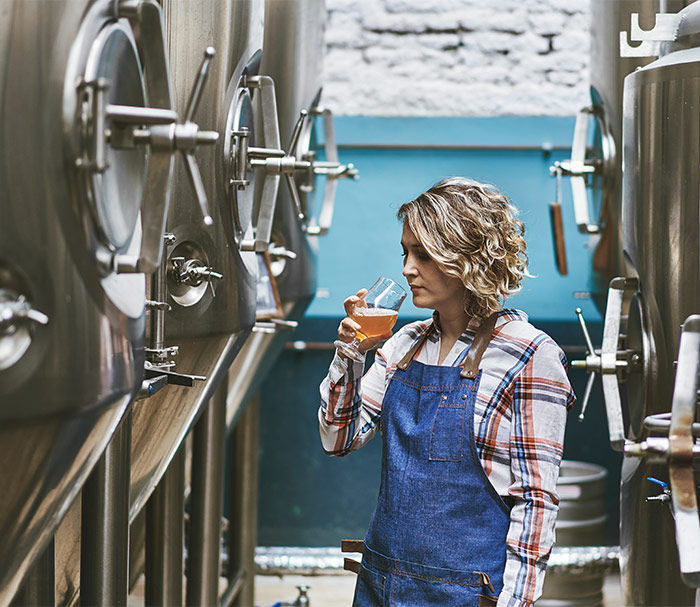 Eine junge Bierbrauerin kostet das Bier in der Produktionshalle.