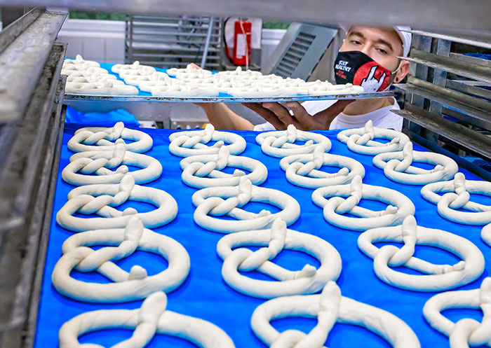 Foto eines Mitarbeiters der Großbäckerei Kistenpfennig in München, der ein Blech roher Brezen über ein anderes schiebt. Der Kunde nutzt PROGAS-Flüssiggas für den Betrieb seiner Öfen