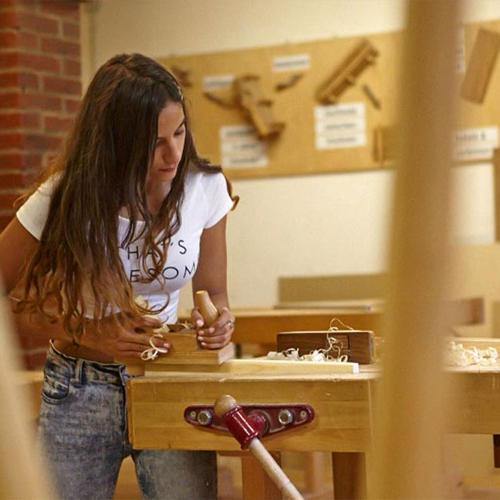 Ein Mädchen bearbeitet einen Block Holz mit einem Hobel.