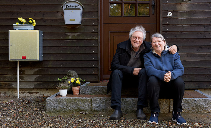 Portrait des Ehepaars, die dicht nebeneinander und fröhlich lachend auf einer Holzstufe ihres Häuschen sitzen.