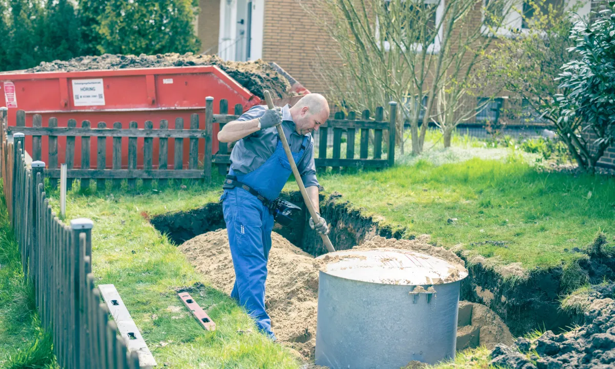 Ein Flüssiggastank wurde in die Grube gelassen und ein Mann verteilt die restliche Erde runf um den Tank.