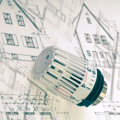 Ein Heizkörperthermostat liegt auf einer Architekturzeichnung eines Hauses