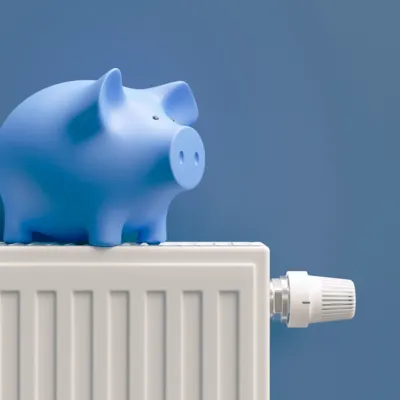 Ein blaues Sparschwein steht auf einem weißen Heizkörper vor einer blauen Wand