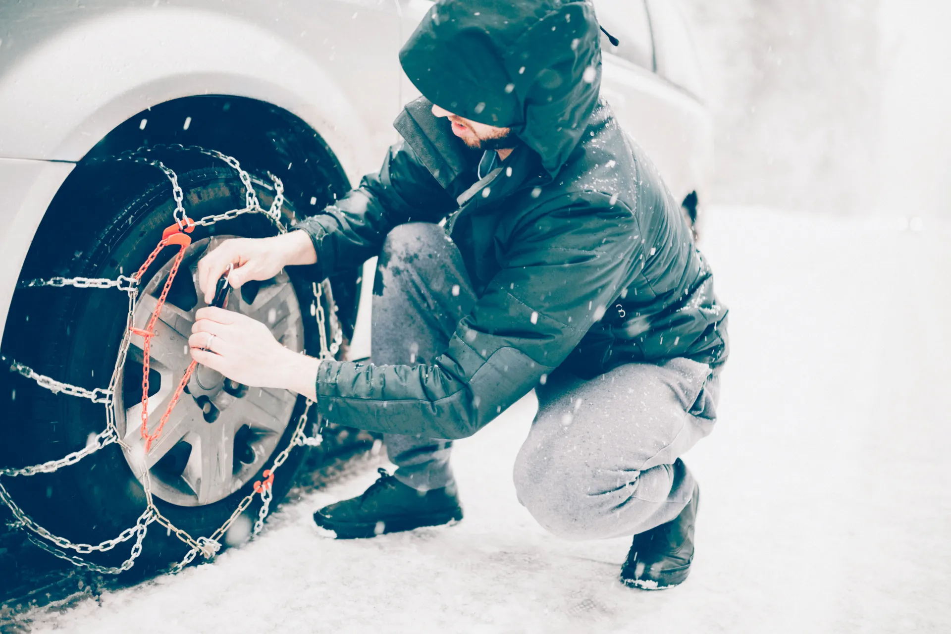Mann befestigt Schneekette an Autoreifen